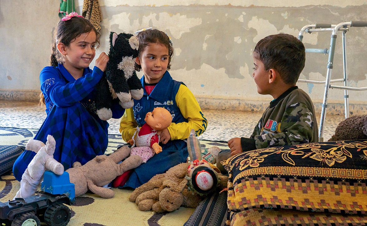 Two girls and a boy, sitting on the floor and playing with stuffed animals.