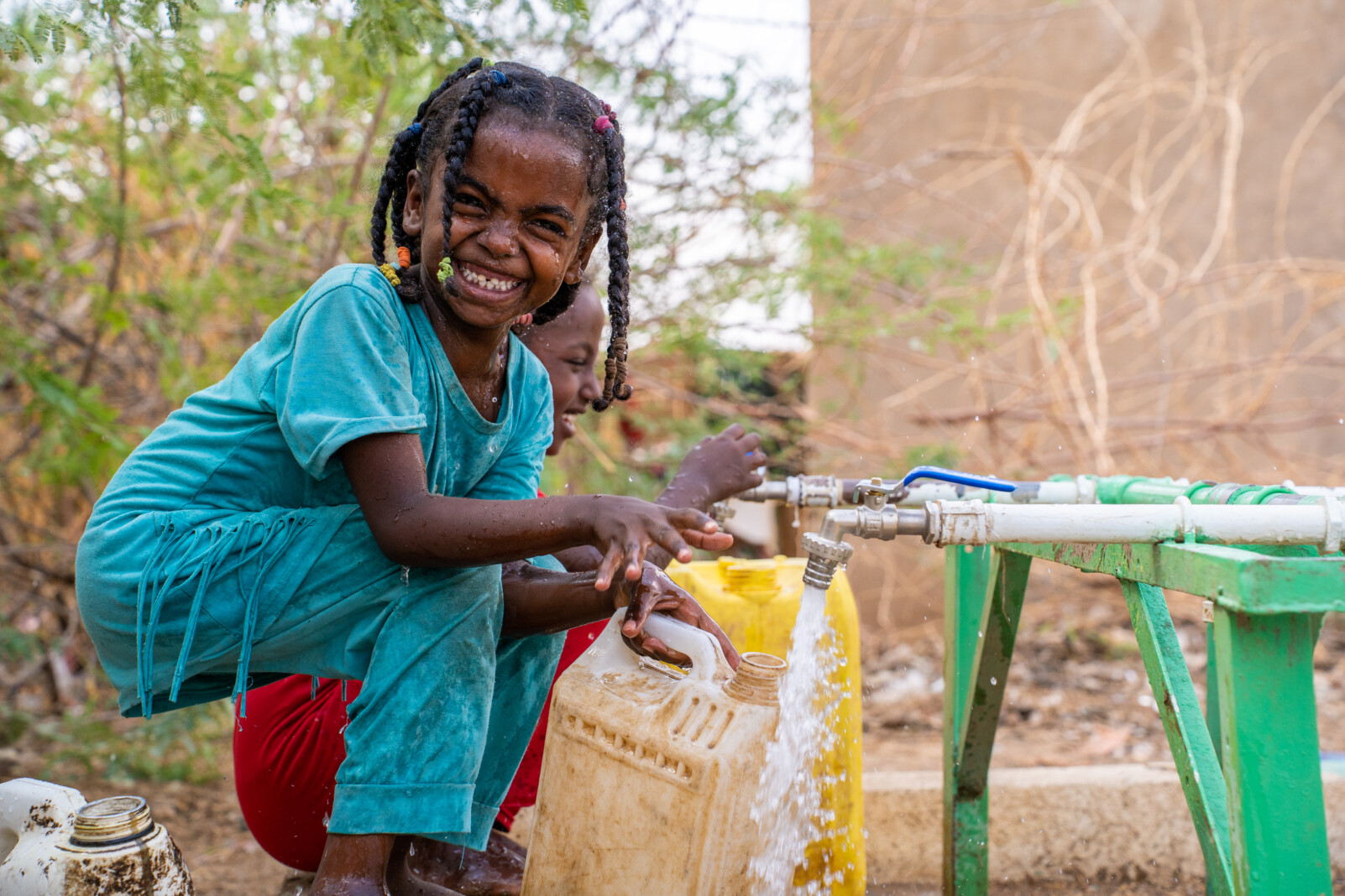 A girl smiling at the camera while fetching water from a rushing tap.